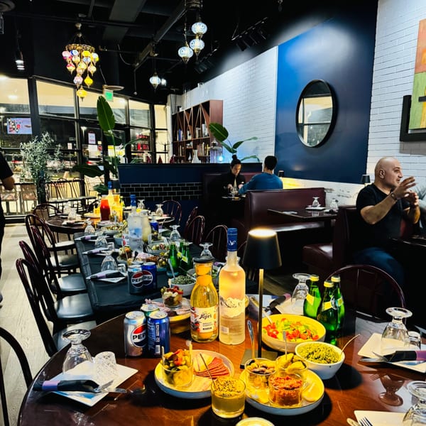 A long table set with Mediterranean appetizers and drinks, with diners in the background at Nora's Grill & Bistro.