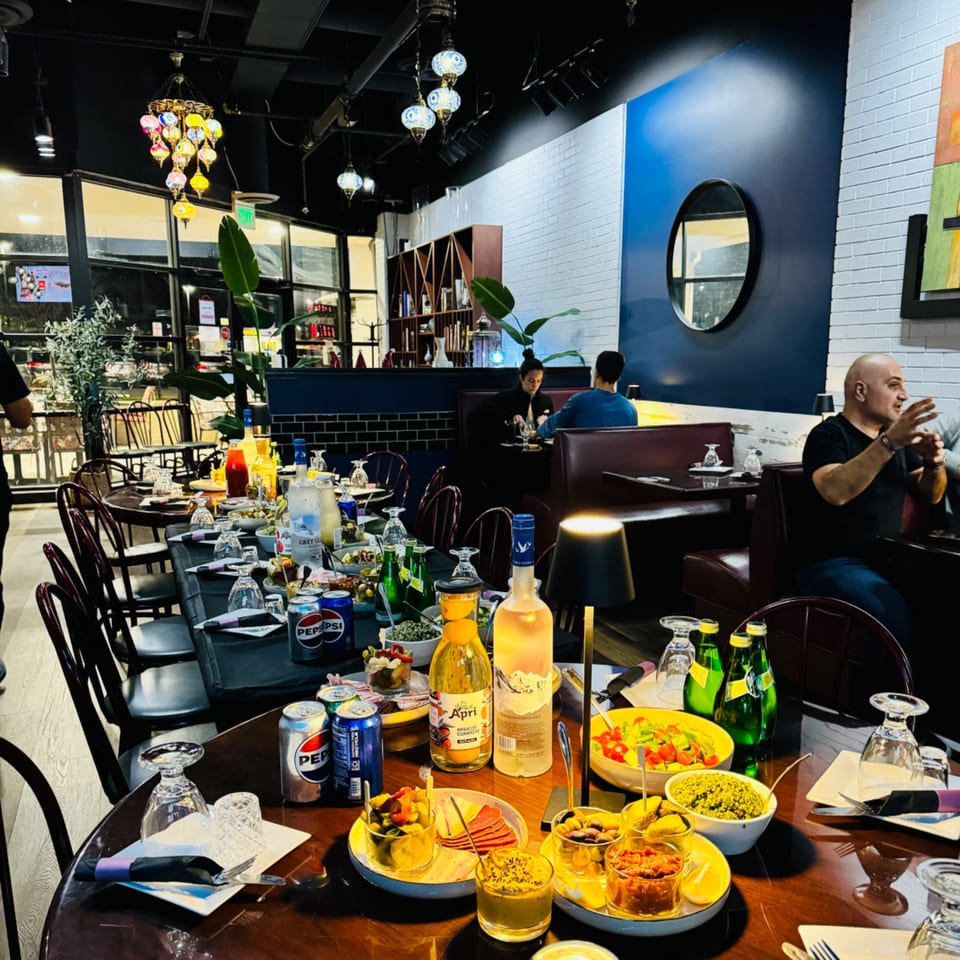 A long table set with Mediterranean appetizers and drinks, with diners in the background at Nora's Grill & Bistro.