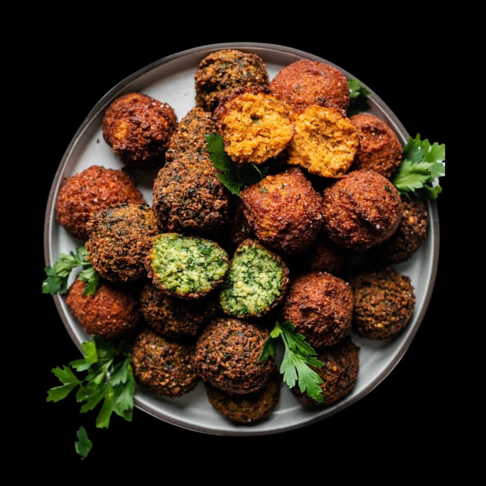 A plate of Nora's Grill & Bistro falafel, some split open revealing green and orange interiors.