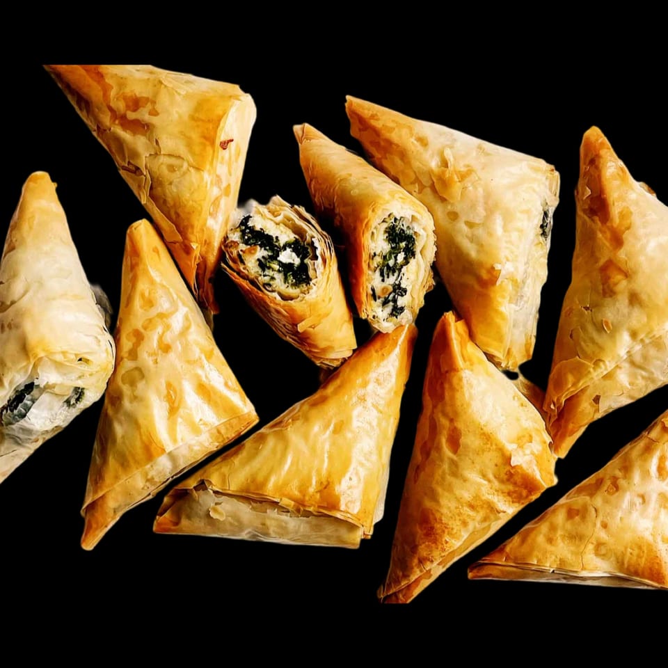 Golden-brown spanakopita triangles with flaky phyllo dough and spinach-feta filling on a black background.