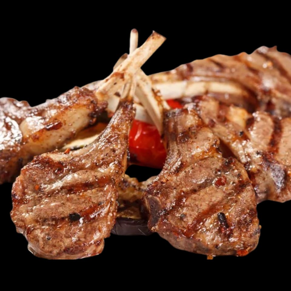 Grilled lamb chops with visible grill marks and red peppers on a dark background.