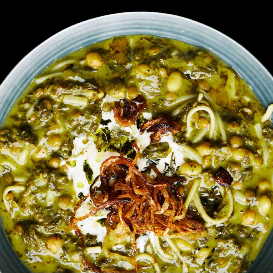 Close-up of a vibrant green Mediterranean stew with noodles, chickpeas, and crispy fried onions.