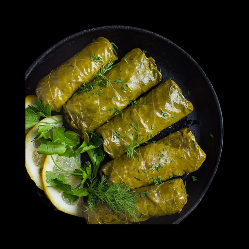 Dolmades, or stuffed grape leaves, garnished with fresh herbs and lemon slices on a dark plate.