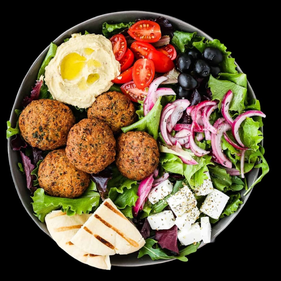 Mediterranean falafel salad with hummus, tomatoes, olives, red onion, feta, and pita bread.