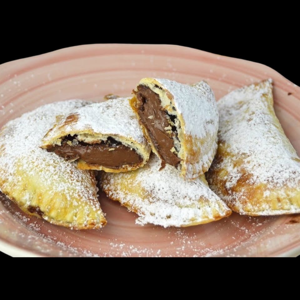 Four chocolate-filled pastries dusted with powdered sugar on a pink plate, one cut open.